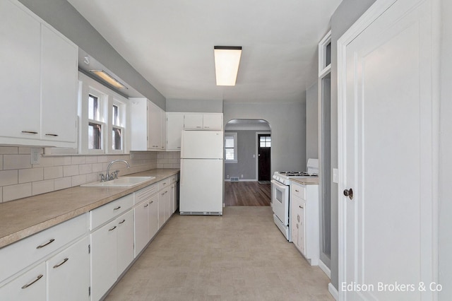 kitchen featuring arched walkways, light countertops, backsplash, white cabinetry, and white appliances