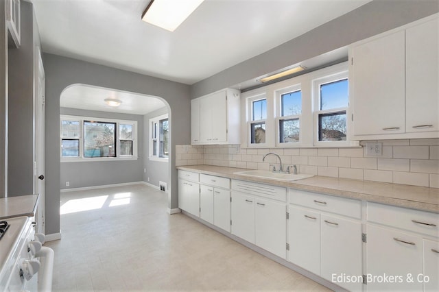 kitchen featuring light countertops, backsplash, white cabinetry, a sink, and white range oven