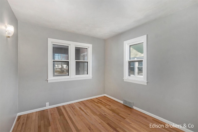 empty room with hardwood / wood-style floors, visible vents, and baseboards