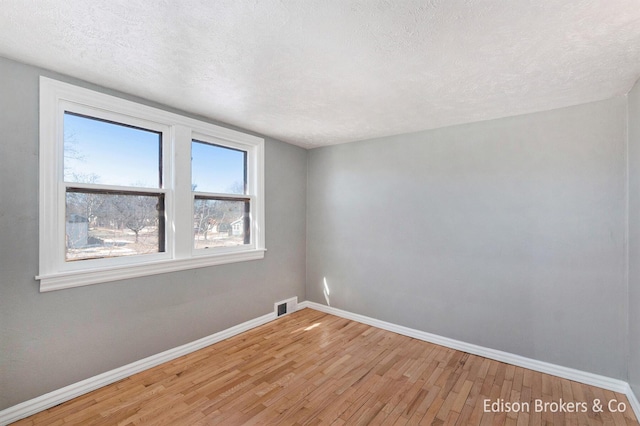 spare room with light wood-style flooring, baseboards, and a textured ceiling