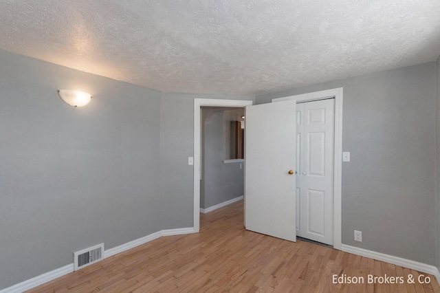 spare room with a textured ceiling, light wood finished floors, visible vents, and baseboards