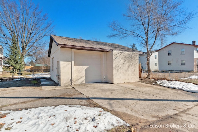 snow covered structure featuring an outbuilding, fence, and driveway