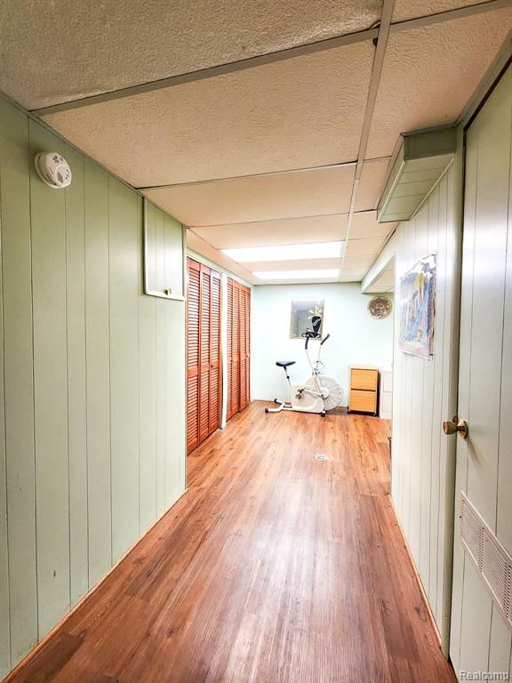 hall featuring wood walls, light wood-style flooring, visible vents, and a drop ceiling