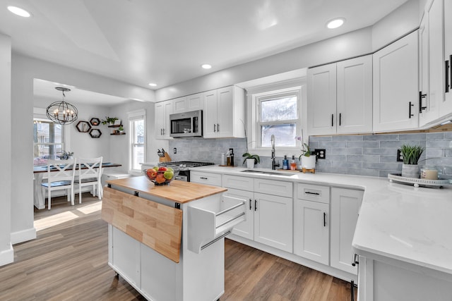 kitchen featuring white cabinetry, stainless steel appliances, a sink, and decorative light fixtures