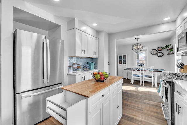 kitchen featuring pendant lighting, stainless steel appliances, tasteful backsplash, white cabinets, and wood finished floors