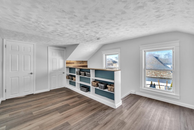 bonus room featuring lofted ceiling, dark wood-style flooring, a textured ceiling, and baseboards