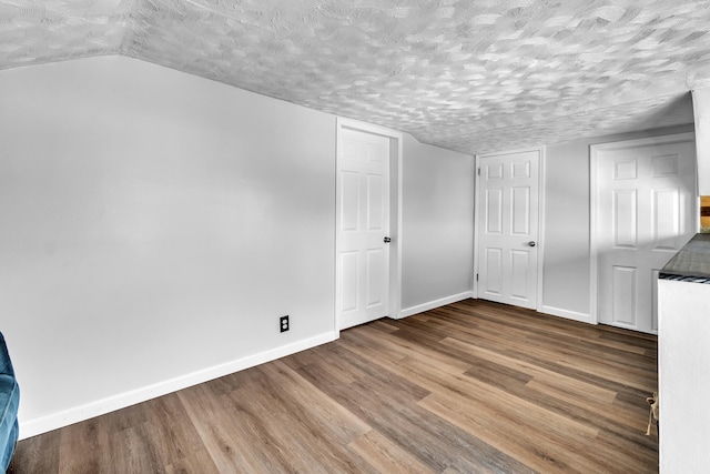 unfurnished bedroom featuring lofted ceiling, baseboards, and wood finished floors