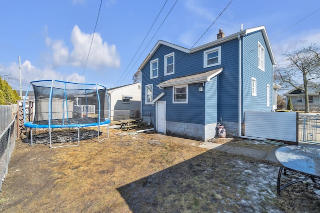 rear view of property featuring a storage shed, a fenced backyard, a chimney, an outbuilding, and a trampoline