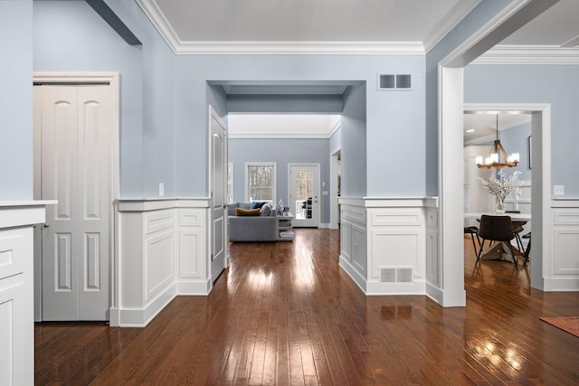 hallway featuring a chandelier, visible vents, wainscoting, dark wood finished floors, and crown molding