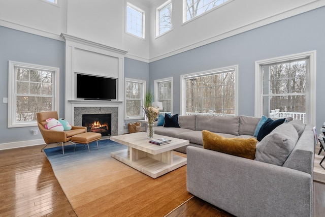 living room with a warm lit fireplace, a high ceiling, dark wood-style flooring, and baseboards