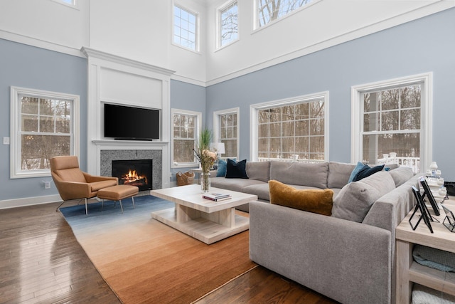 living room featuring dark wood-type flooring, a high ceiling, a lit fireplace, and baseboards