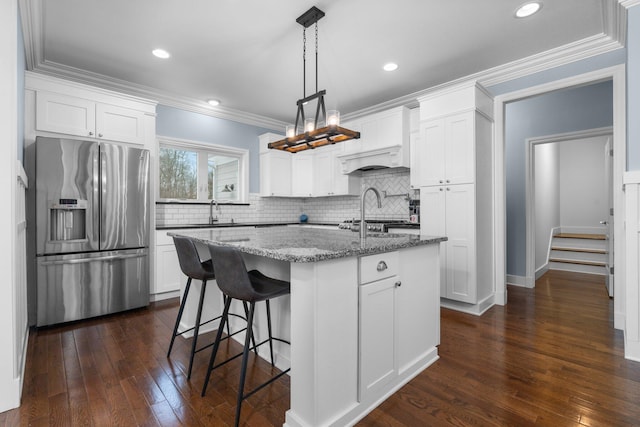 kitchen with pendant lighting, a kitchen island with sink, stainless steel fridge with ice dispenser, and white cabinetry