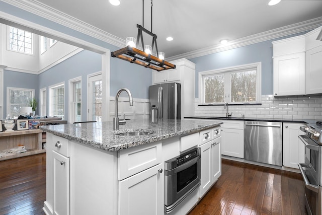 kitchen with appliances with stainless steel finishes, white cabinets, a sink, and an island with sink