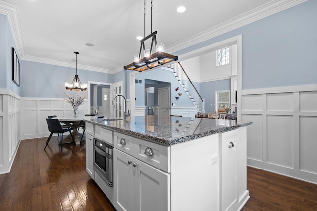 kitchen featuring an island with sink, a sink, decorative light fixtures, and white cabinets