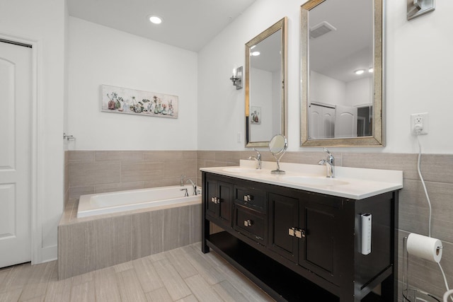 bathroom featuring double vanity, tiled tub, a sink, and tile walls