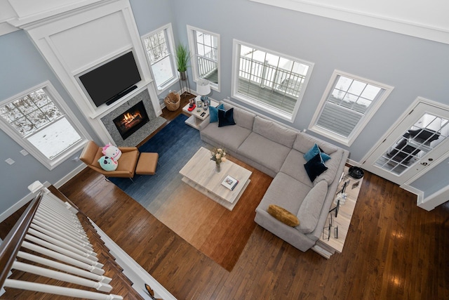 living room featuring a warm lit fireplace, a healthy amount of sunlight, and dark wood-style flooring