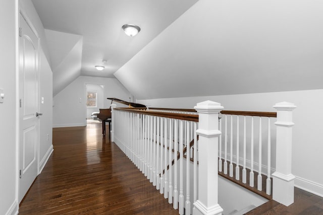 hallway featuring baseboards, vaulted ceiling, dark wood-style flooring, and an upstairs landing