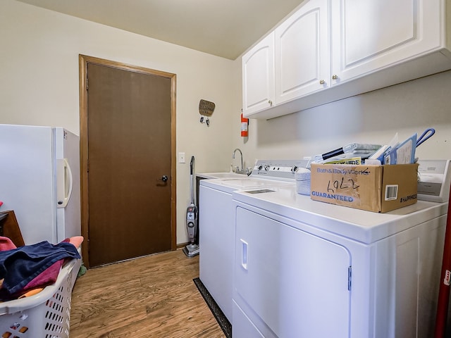 laundry area featuring cabinet space, light wood-style flooring, a sink, and washing machine and clothes dryer