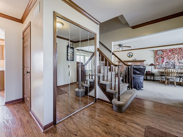 staircase with baseboards, visible vents, ornamental molding, wood finished floors, and a textured ceiling