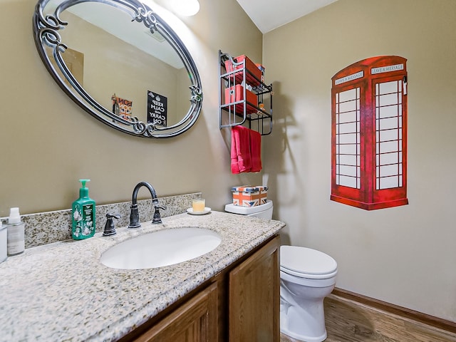 half bathroom with toilet, baseboards, wood finished floors, and vanity