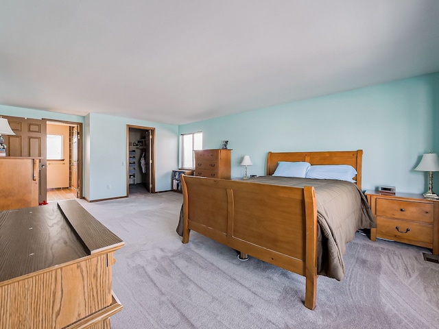 bedroom featuring a spacious closet, a closet, ensuite bath, and light colored carpet