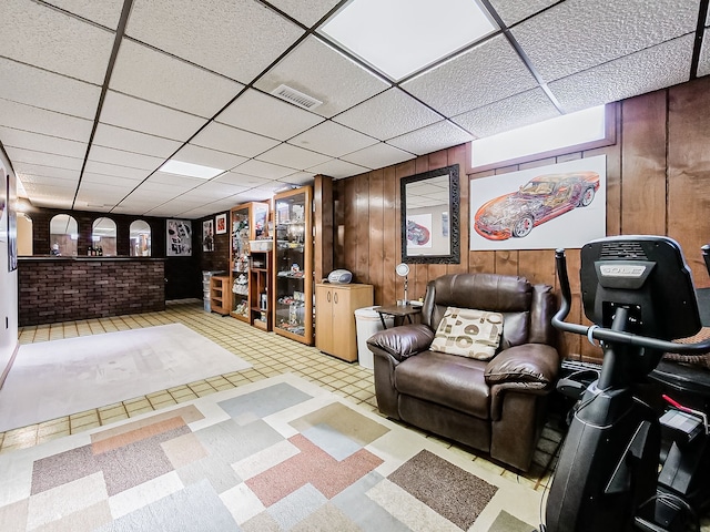 unfurnished living room featuring visible vents, a drop ceiling, wooden walls, and light floors