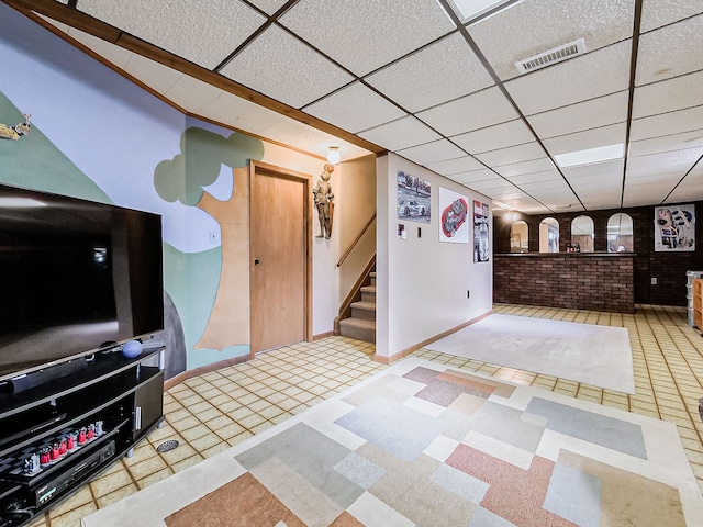 interior space with visible vents, baseboards, brick wall, stairway, and a paneled ceiling