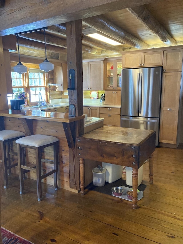 kitchen featuring rustic walls, hardwood / wood-style flooring, glass insert cabinets, beamed ceiling, and freestanding refrigerator