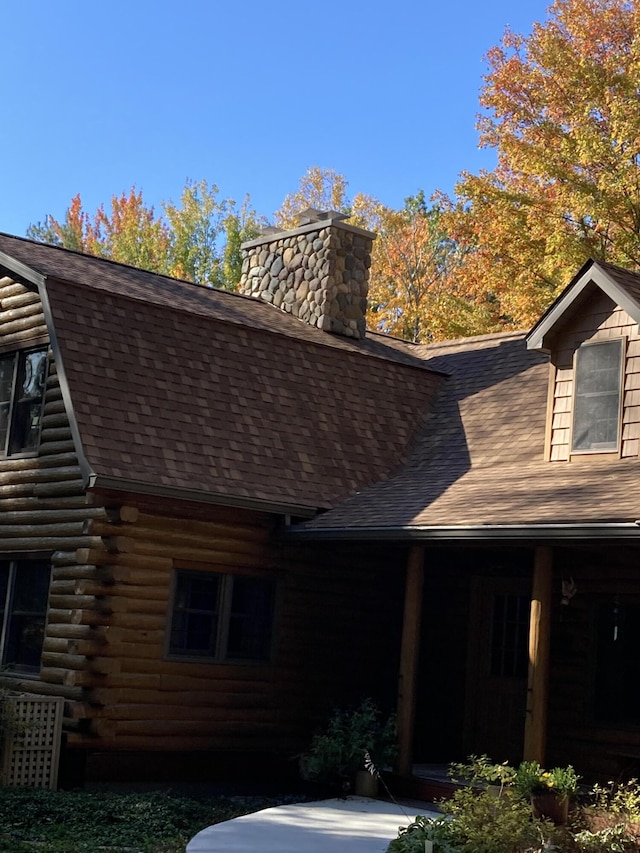 exterior space featuring roof with shingles, a chimney, and log siding