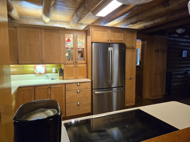 kitchen with black electric stovetop, beam ceiling, brown cabinetry, and freestanding refrigerator