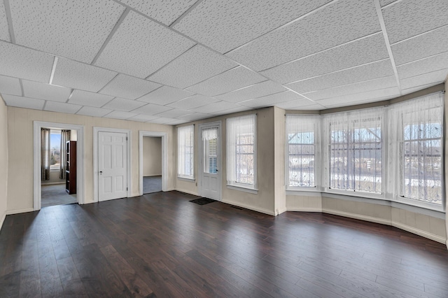 spare room featuring baseboards, a drop ceiling, and dark wood-type flooring