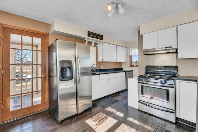 kitchen with stainless steel appliances, dark countertops, white cabinetry, and under cabinet range hood