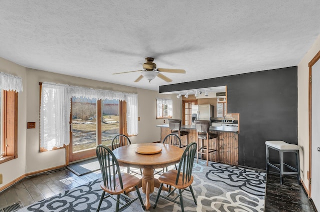 dining area featuring dark wood-style flooring, visible vents, a ceiling fan, track lighting, and baseboards