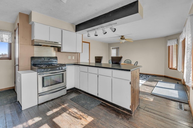 kitchen with a peninsula, under cabinet range hood, white cabinets, and gas stove