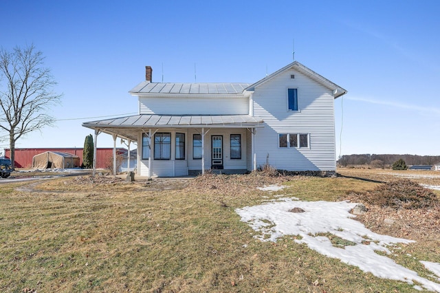 view of front facade with a chimney, a porch, a standing seam roof, metal roof, and a front lawn