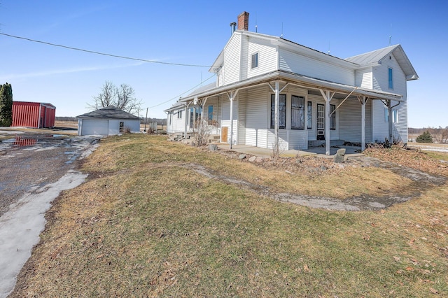 view of side of home featuring a yard, a detached garage, a porch, and an outdoor structure