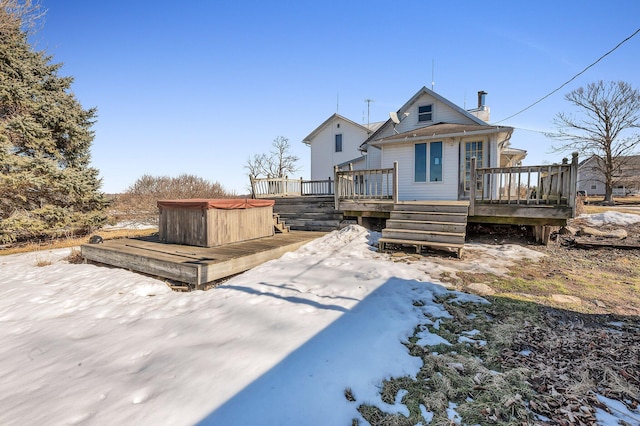 snow covered house with a deck, a chimney, and a hot tub