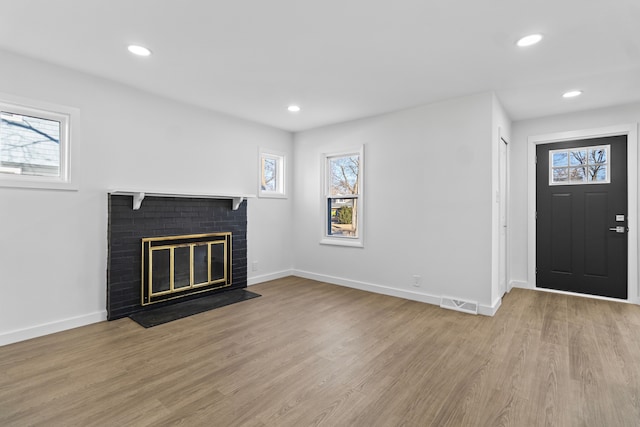 unfurnished living room featuring a brick fireplace, plenty of natural light, and wood finished floors