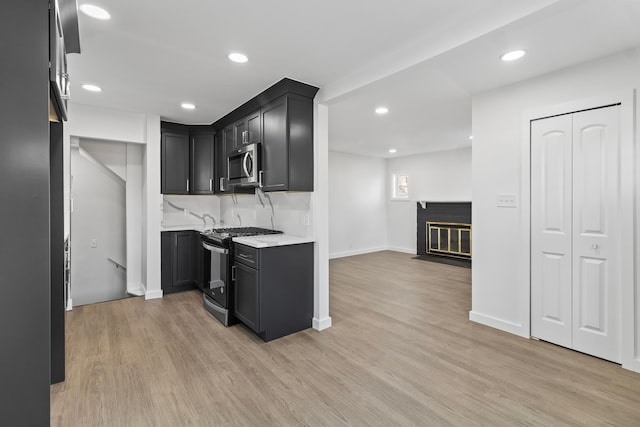 kitchen with light wood-style flooring, stainless steel microwave, gas range, and decorative backsplash