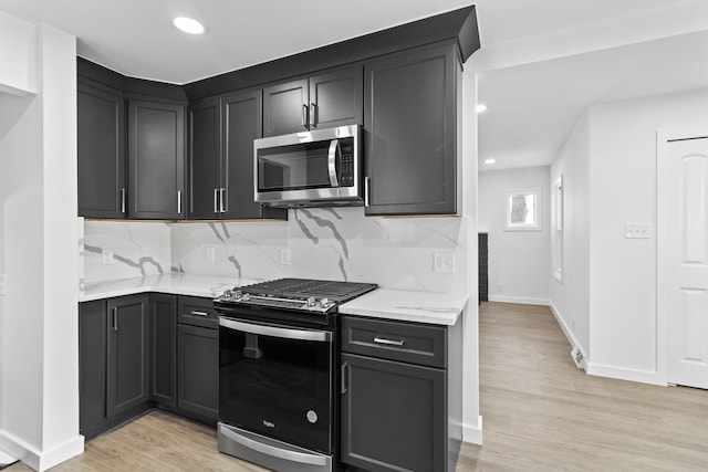 kitchen with light wood-type flooring, appliances with stainless steel finishes, decorative backsplash, and recessed lighting