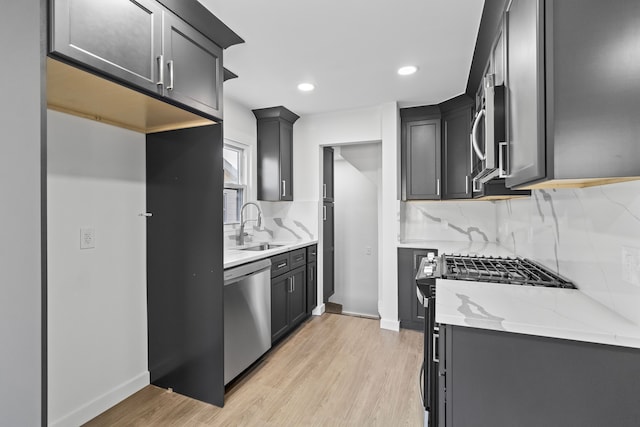 kitchen with light wood-style flooring, light stone counters, stainless steel appliances, and a sink