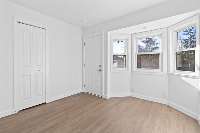 unfurnished bedroom featuring light wood-type flooring, baseboards, and a closet