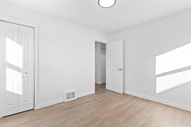 unfurnished bedroom featuring a closet, visible vents, baseboards, and wood finished floors