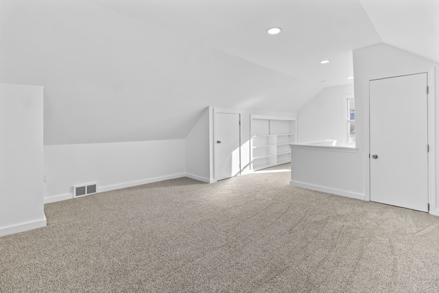 additional living space featuring vaulted ceiling, carpet floors, built in shelves, and visible vents