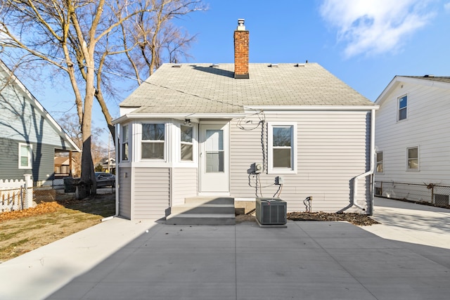 back of property featuring a shingled roof, fence, a chimney, and central AC unit