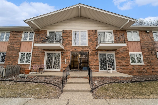 view of front of home with a balcony, a patio, and brick siding