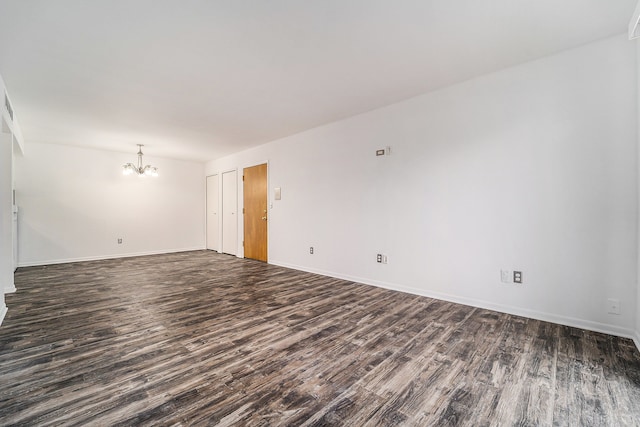 spare room with baseboards, a chandelier, and dark wood-style flooring