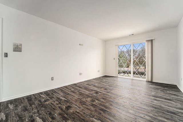 empty room with dark wood finished floors, visible vents, and baseboards