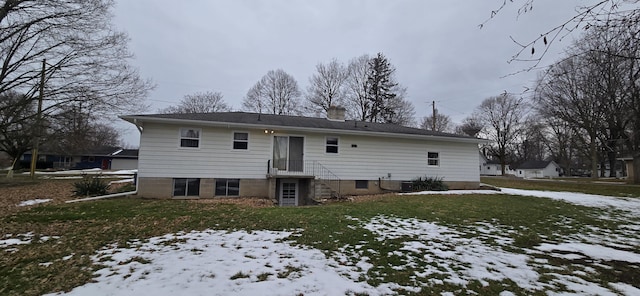 snow covered rear of property with cooling unit, a yard, and a chimney