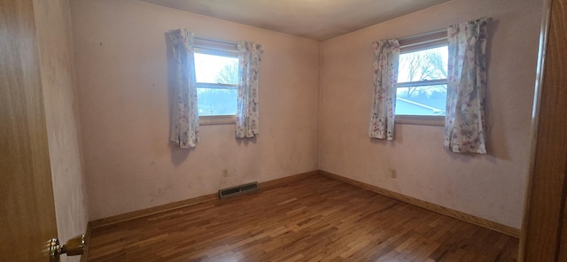 spare room with baseboards, hardwood / wood-style floors, visible vents, and a healthy amount of sunlight